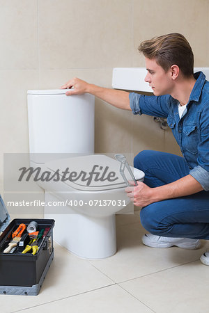 Side view of a handsome plumber with toolbox doing toilet reparation