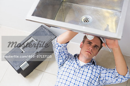 Young plumber repairing washbasin drain in bathroom