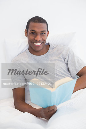 Portrait of a smiling young Afro man with a book in bed at house