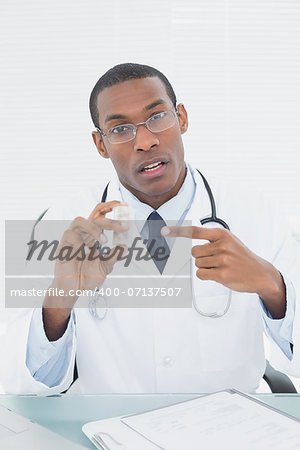 Portrait of a male doctor pointing at prescription bottle in medical office