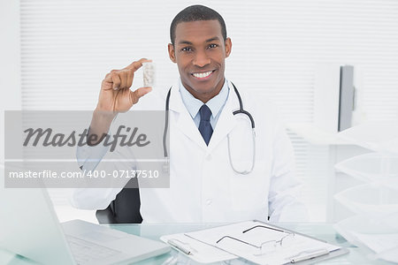 Portrait of a smiling male doctor holding a prescription bottle in medical office