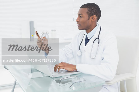 Side view of a male doctor text messaging while using laptop at medical office