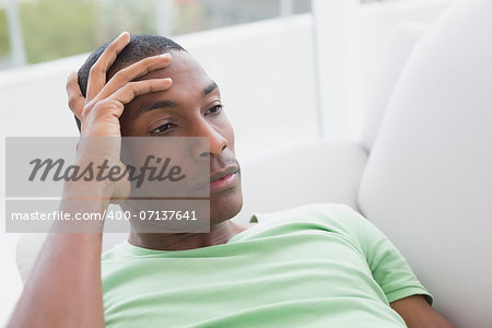 Close up of a thoughtful relaxed young Afro man lying on sofa in a house