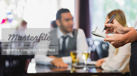 Waitress writing an order in front of two business people talking