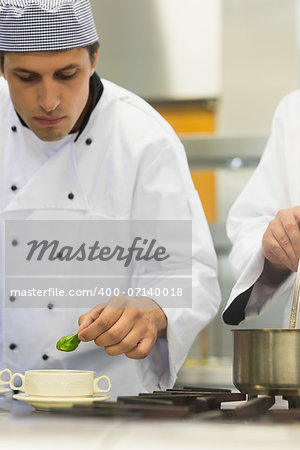 Young male chef garnishing a bowl soup with a basil leaf in kitchen