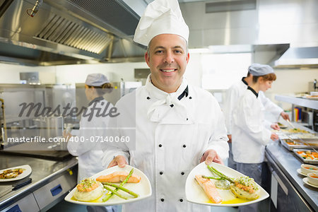 Mature head chef presenting proudly some dinner plates in a busy kitchen