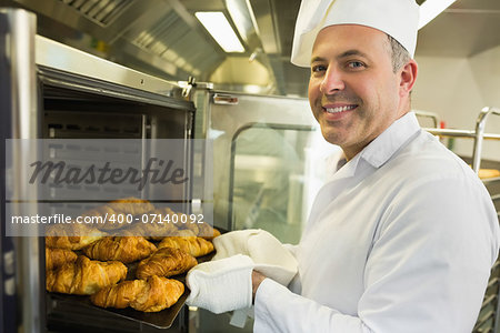 Mature baker smiling proudly at the camera take some croissants out of oven