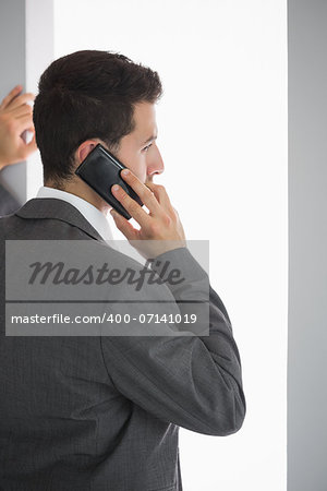 Rear view of stern businessman standing in front of window phoning in bright room