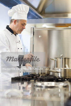 Concentrating head chef stirring in pot in professional kitchen