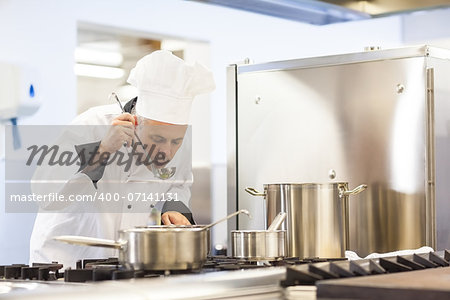 Focused head chef tasting food from ladle in professional kitchen