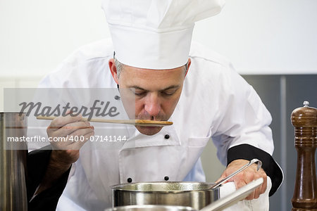 Focused head chef tasting sauce with wooden spoon in professional kitchen