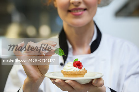 Happy head chef putting mint leaf on little cake on plate in professional kitchen