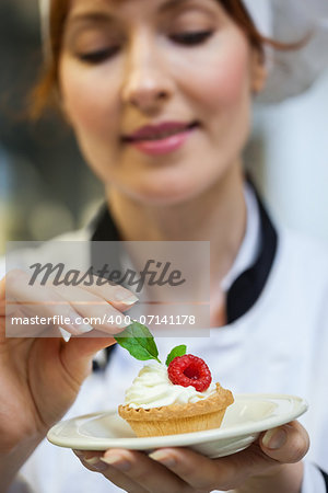 Focused head chef putting mint leaf on little cake on plate in professional kitchen