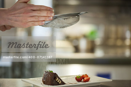Chef finishing a dessert plate with icing sugar