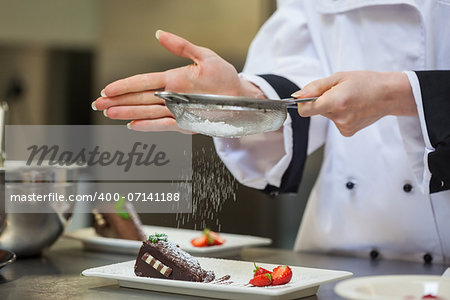 Female chef finishing a dessert plate with icing sugar
