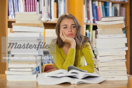 Thoughtful pretty student studying between piles of books in library