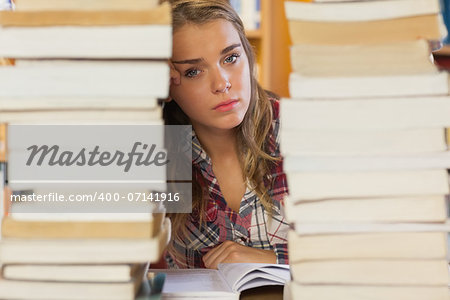 Stern pretty student studying between piles of books in library