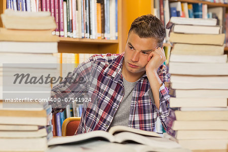 Frustrated handsome student studying between piles of books in library