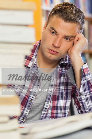 Tired handsome student studying between piles of books in library