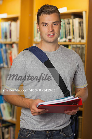 Handsome smiling student holding folder and notebooks in library
