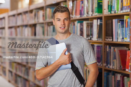 Handsome smiling student holding tablet in library