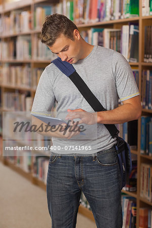 Handsome serious student looking at tablet in library