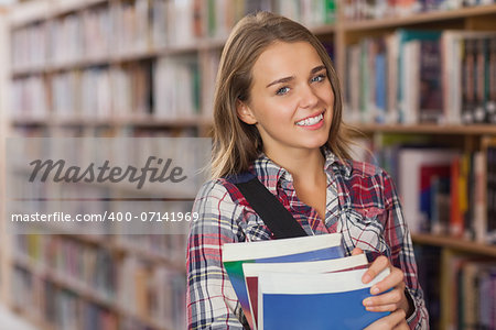 Pretty smiling student holding books in library