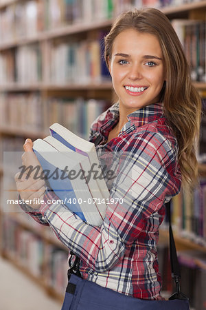 Pretty cheerful student holding books in library