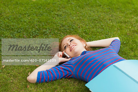 Gorgeous smiling student lying on grass phoning on campus at college