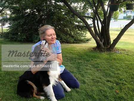 Mature woman kneeling on grass with dog, smiling