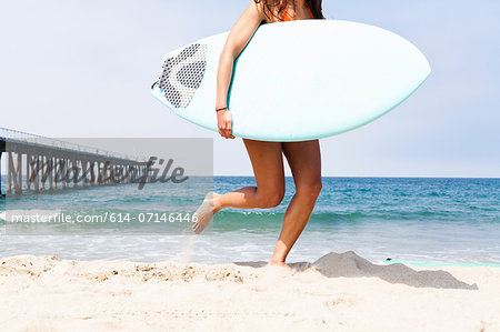 Woman running with surfboard, Hermosa Beach, California, USA