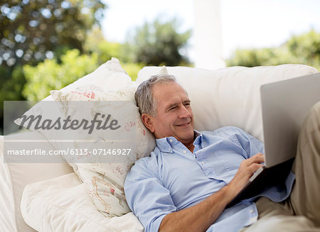 Senior man using laptop on patio sofa