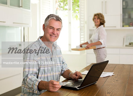 Portrait of smiling senior man using laptop in kitchen