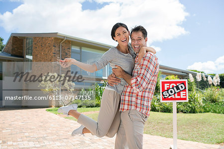 Portrait of enthusiastic couple hugging outside house with For Sale sign Portrait of enthusiastic couple hugging outside house with For Sale sign