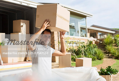 Man holding cardboard box overhead near moving van in driveway