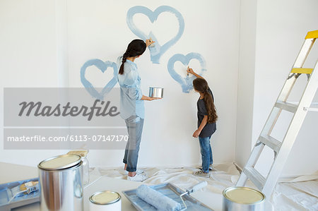 Mother and daughter painting blue hearts on wall in new house