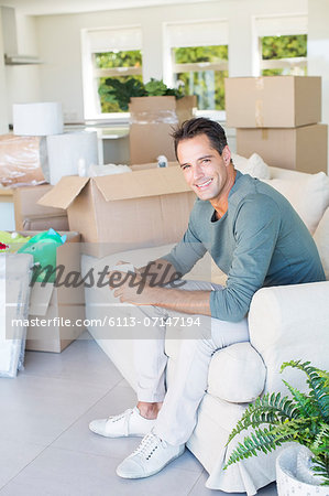 Portrait of smiling man enjoying coffee on sofa among cardboard boxes