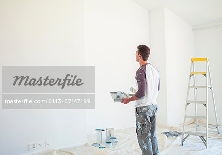 Man with paint tray looking up at white wall