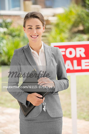 Portrait of smiling realtor near For Sale sign