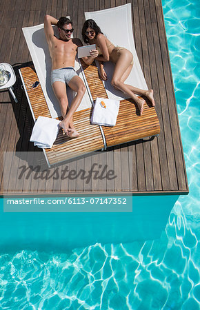 Couple relaxing on lounge chairs at poolside