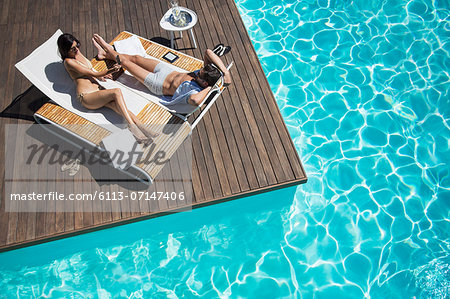 Couple laying on lounge chair at poolside