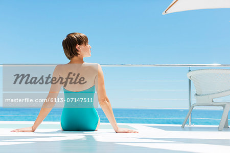 Woman relaxing poolside with ocean in background