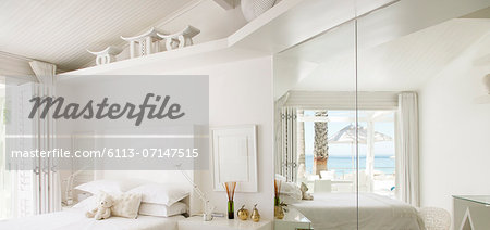 Reflection of beach and ocean in mirror of white bedroom