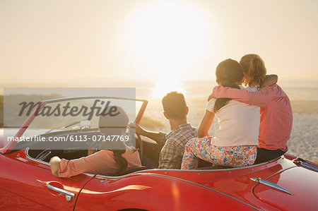 Family watching sunset over ocean from convertible on beach Family watching sunset over ocean from convertible on beach