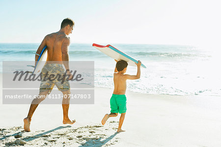 Father and son carrying surfboard and bodyboard on beach