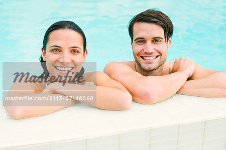 Portrait of smiling couple leaning at edge of swimming pool