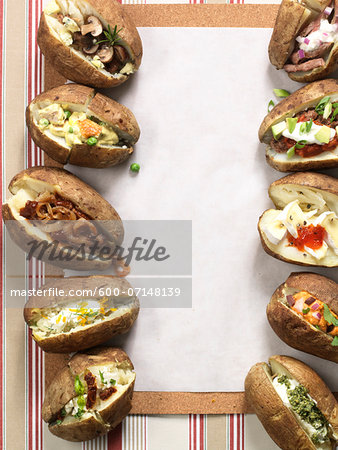 Several baked potatoes with a variety of toppings, studio shot