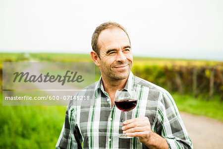 Portrait of vintner standing in vineyard, holding glass of wine, Rhineland-Palatinate, Germany