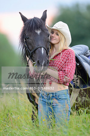 Young woman standing beside a horse on a meadow