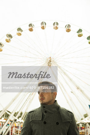 Portrait of young man standing in front of ferris wheel at amusement park, Germany